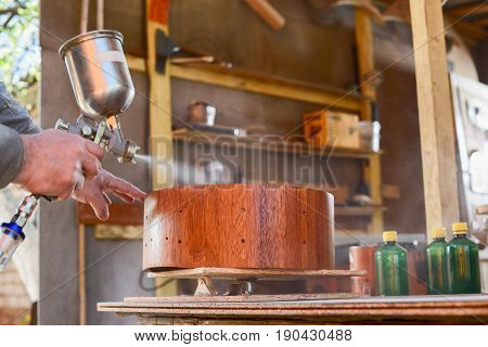 Carpenter spraying lacquer on merbau wood drum shell at workshop