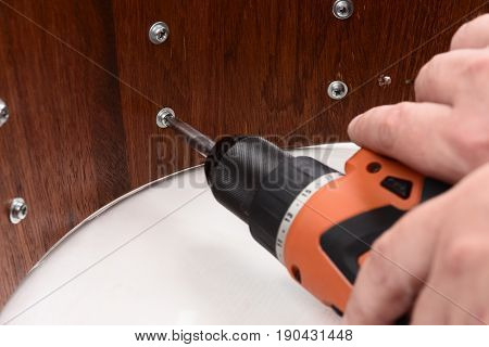 Carpenter tightening screws on wooden drum shell with electric screwdriver closeup