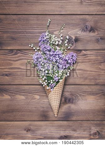 Waffle cone with lily of the valley lilak flowers on wooden background
