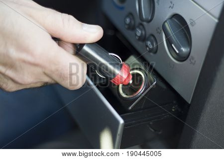 Hand inserts the plug into the 12V socket from the car's cigarette lighter.