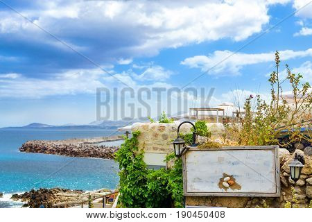 White signboard on stone wall of outdoor resort cafe on top of hill above highway along promenade Emmanouil Kefalogianni. Greek architecture on coast of Kolpos Almirou. Rethymno Crete Greece