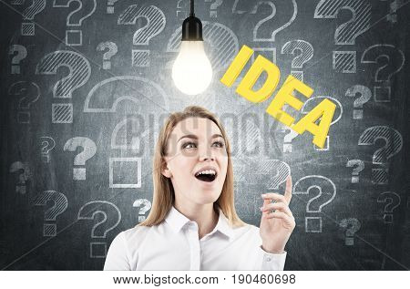 Portrait of a blond businesswoman wearing a white shirt and having an aha moment near a blackboard with a business idea sketch on it.