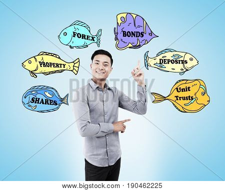 Cheerful Asian business guru is standing against a light blue background with business buzzwords written on fish of different colors.