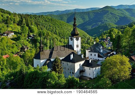 Spring in Slovakia. Old mining village. Historic church in Spania dolina. Springtime colored trees at sunset.