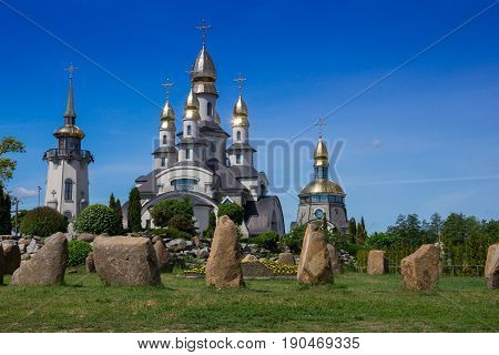White church with domes on a blue sky background and boulders on a foreground. Mezhyhirya Residence in Ukraine