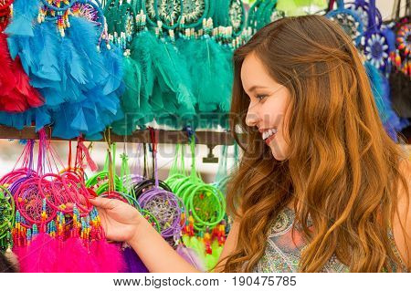 Close up of a beautiful smiling young woman touching a colorful catchdreamers, in colorful market fabrics background.