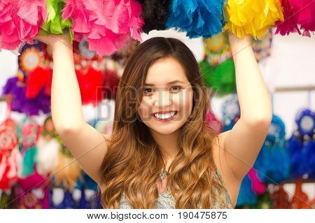 Close up of a beautiful smiling young woman touching a colorful catchdreamers, in colorful market fabrics background.