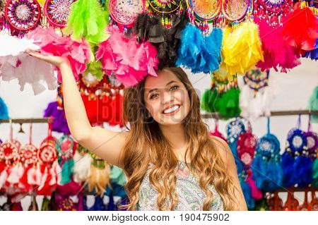 Beautiful smiling young woman touching a colorful catchdreamers, in colorful market fabrics background.