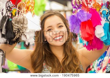 Close up of a beautiful smiling young woman hiding behind a colorful catchdreamer, in colorful market fabrics background.