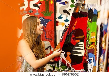 Beautiful smiling young woman with humbs up and posing for camera, with colorful andean traditional clothing fabrics background.