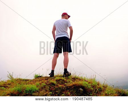 Man In Cloud Of Fog. Hiker In White Black With  Red Cap Stand On Peak .