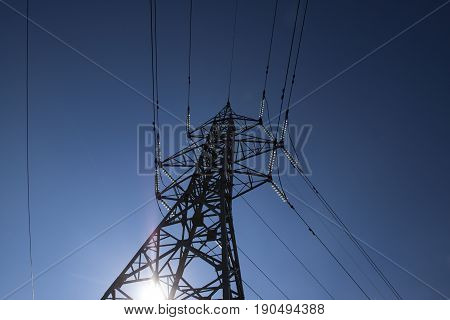 High voltage power pylons against blue sky and sun rays high-voltage power lines at sunrise.