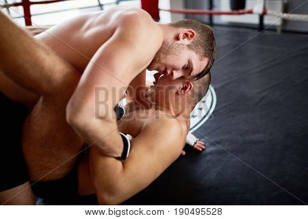Portrait of shirtless wrestlers fighting in boxing ring: tackling opponent to floor and performing submission hold