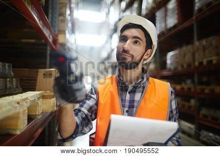Worker with scanner standing by shelves with goods