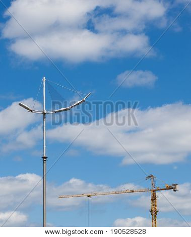 high construction crane and city light stand pole against the background of the blue sky and clouds