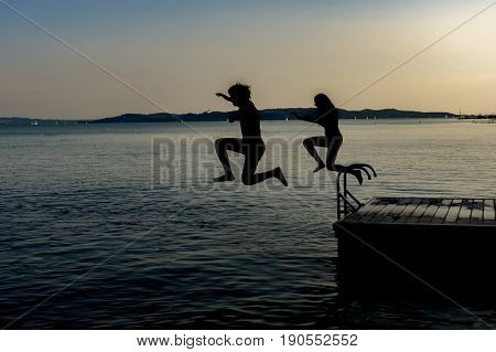 Shiluette of boy and girl jumping in the lake from pier