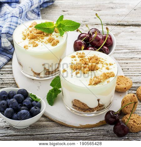 Healthy summer dessert of berry yogurt almond cookies portioned in glass cups on a light wooden background with ripe blueberries and juicy cherries. Selective focus. the concept of fitness nutrition.