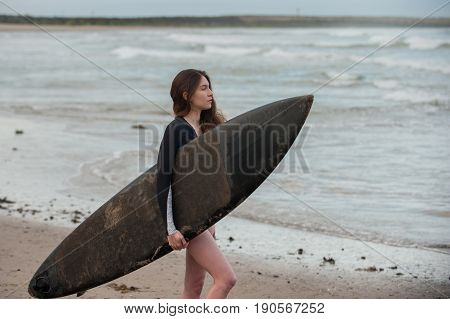 Sexy California surfer girl in landscape view holding surf board under arm while checking the waves.