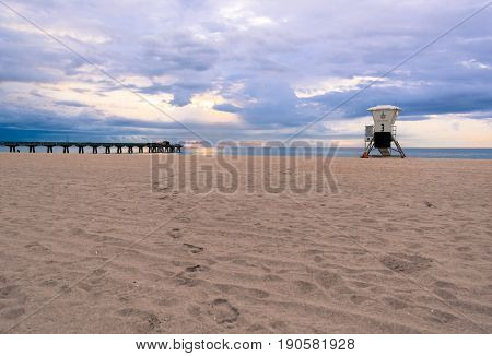 footprints in the sand on an empty florida beach on a cloudy summer morning at sunrise between the pier and lifeguard stand