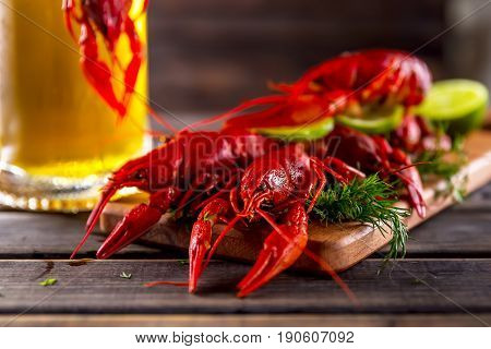 Boiled crayfishes with greens and lime on a wooden background.Nearby glass of beer . Snack to beer. Summer atmosphere. Selective focus