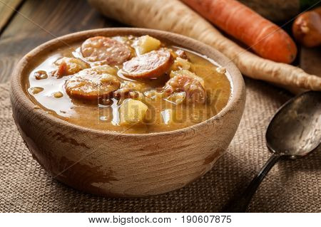 Wooden Bowl Of Split Pea Soup With Sausage And Potatoes