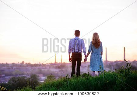 Young Couple Is Holding Hands On A Background Sunset