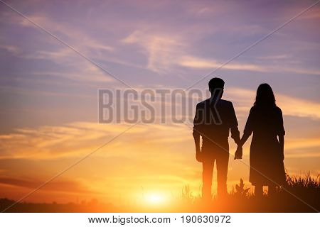 Young Couple Is Holding Hands On A Background Sunset Silhouette