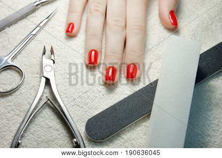 nail scissors file and clippers to remove the cuticle care products on white towel with woman manicured red nails