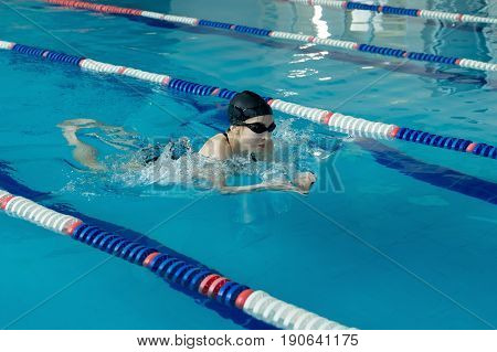Young Woman In Goggles And Cap Swimming Breaststroke Stroke Style In The Blue Water Indoor Race Pool