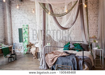 Modern loft bedroom with high ceiling, brick wall, wood floor, wooden cabinet, design accessories in the steel stack, dining table with chairs. Mock up interior photo