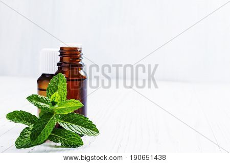 Essential oil of peppermint in dark bottles  on white wooden background selective focus