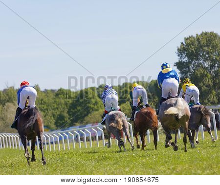 STOCKHOLM SWEDEN - JUNE 06 2017: Rear view of standing colorful jockeys on gallop race horses riding in a curve at Nationaldags Galoppen at Gardet. June 6 2017 in Stockholm Sweden