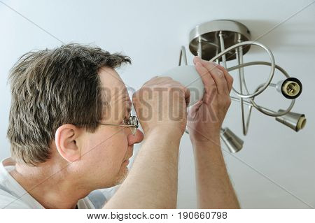 Electrician is installing a LED light bulb in a ceiling lamp.