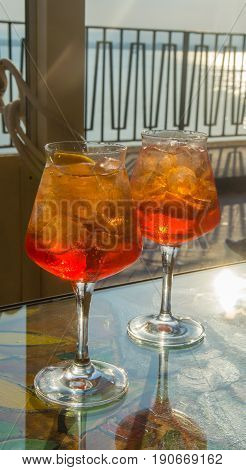 Waiter prepared the Aperol Sprits summer cocktail with Aperol prosecco ice cubes and orange in wine glass ready to drink on sunny terrace with sea view