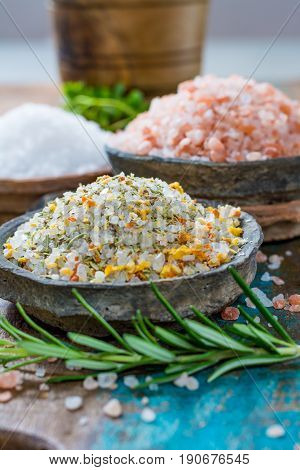Different types of natural salt in stone bowls on wooden surface. White sea salt pink Himalayan salt Spiced salt with rosemary