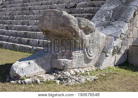 Closeup of stone serpent head sculpture at bottom of rock stairway of El Castillo pyramid on sunny day at Chichen Itza in Yucatan Mexico