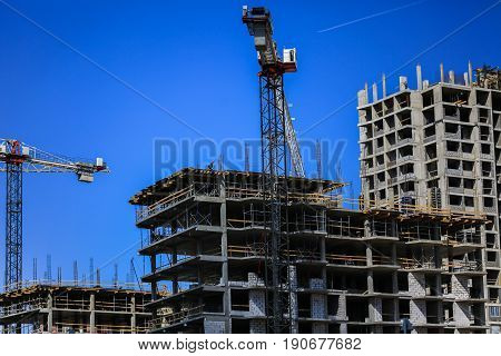 Construction concept. A new building under construction against the sky. Blue background. New urban city. Machinery, cranes and builders on scaffolding. Heavy industry and safety at work.