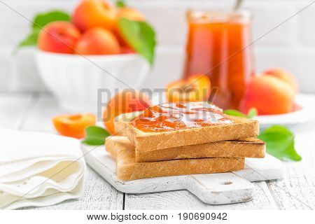 Toasts of bread with apricot jam and fresh fruit with leaves on white wooden table. Tasty breakfast.