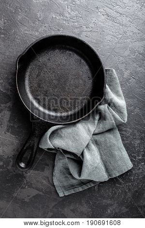 Empty cast iron frying pan on dark grey culinary background view from above