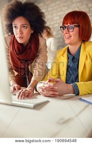 Afro-American girl in office adjusts computer to female co-worker colleague 