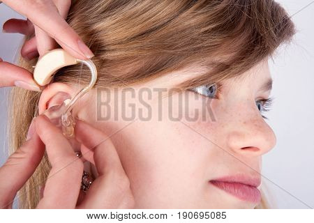 Close up of a young girl's head and the audiologist's hands inserting hearing aid into ear