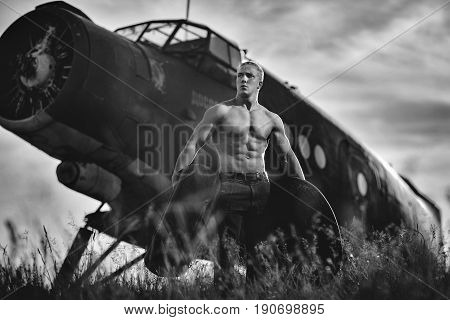 A handsome guy with tires in his hands is standing by the plane. Black and white photo.