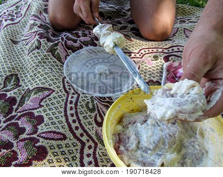 Male hands stick the beautiful juicy Meat in marinade to the skewer close-up. Preparation of the pork and beef meat for frying at the campfire
