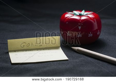 Mechanical Tomato shaped kitchen timer for cooking studying and working with pencil and goal list.