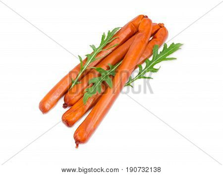 Several long thin smoked hunting frankfurters in the natural casing with several arugula leaves on a light background