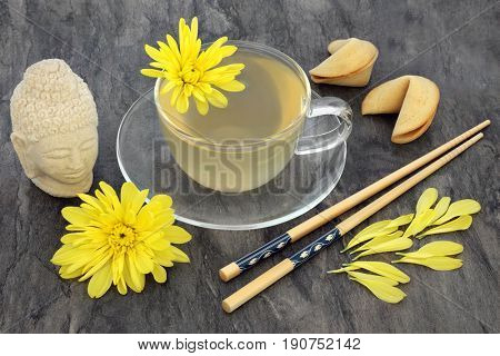 Chrysanthemum herb flower tea with glass cup, fortune cookies, chopsticks and stone Buddha head. Also used in traditional Chinese and Japanese herbal medicine.