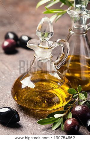 Olive oil in a glass bottle and olive branch on brown stone table