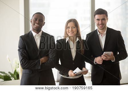 Cheerful businesswoman in formal wear standing between two confident businessmen posing for camera, multi-ethnic team portrait, motivated professional consultants, board of directors, business group