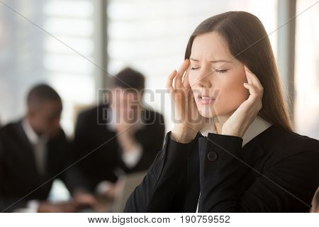 Young frustrated businesswoman feels unwell dizzy during meeting, touching massaging temples, trying to cope with migraine, chronic headache caused by physical emotional work stress, nervous disorder