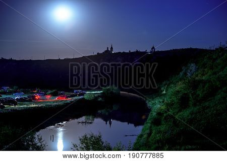 Wonderful landscape with rocks and mountains at orheiul vechi memorial in moldova, night view with full moon and reflection in the raut river and monastery with church and cars